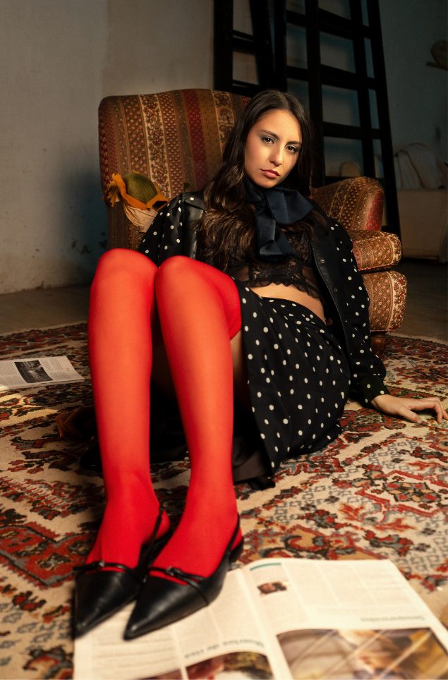 Modelo con medias rojas sentada en un sillón sobre una alfombra