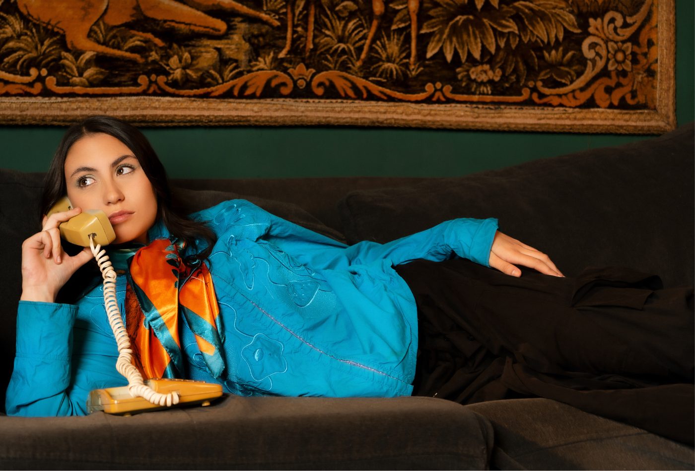 Modelo recostada en un sillón con campera celeste y teléfono antiguo