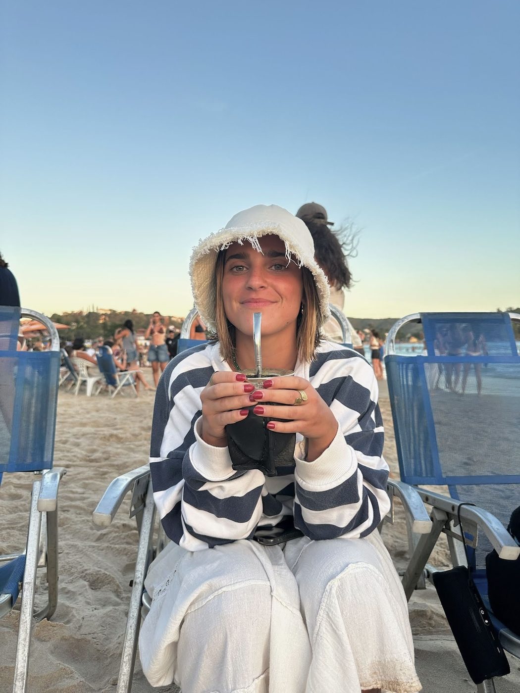 Milagros tomando mate en la playa con gorro